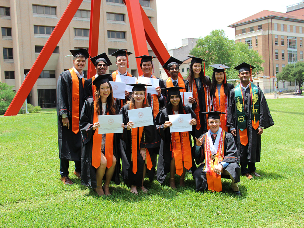 A group of male and female Texas ChE students stand on the front lawn of the CPE building in their cap and gowns after graduation.