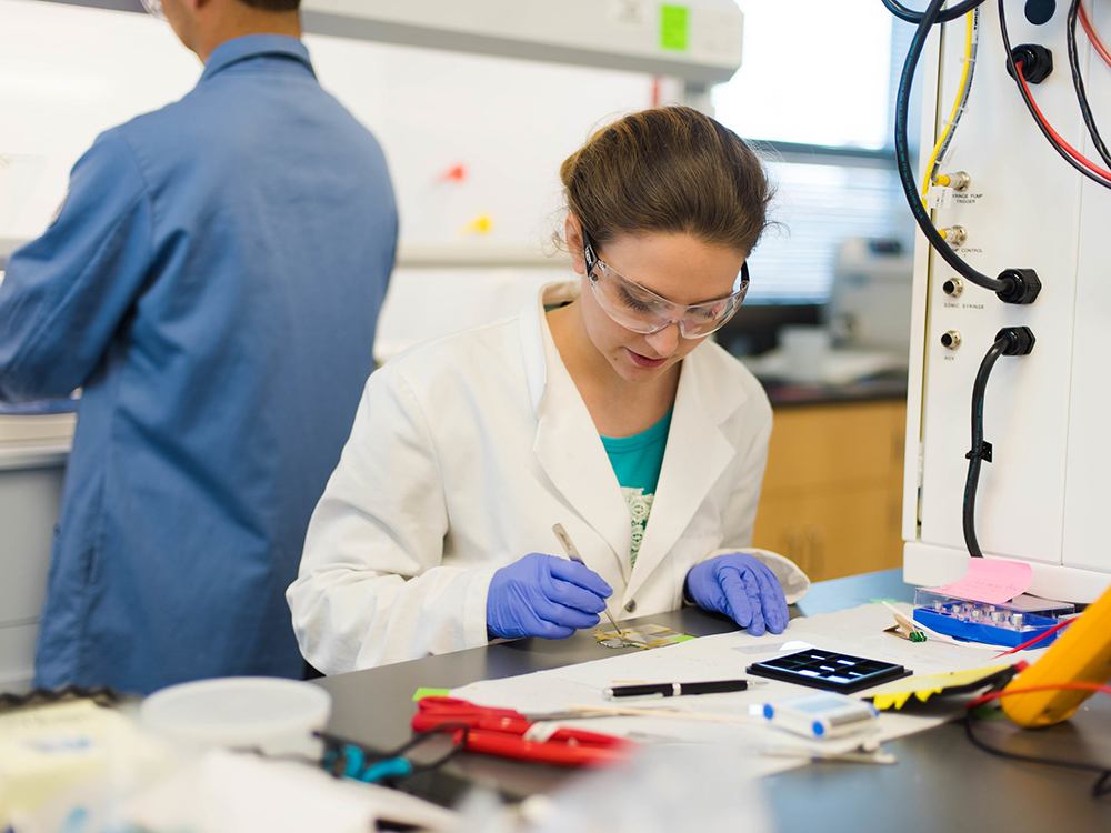 woman sitting in lab with small devices at desk