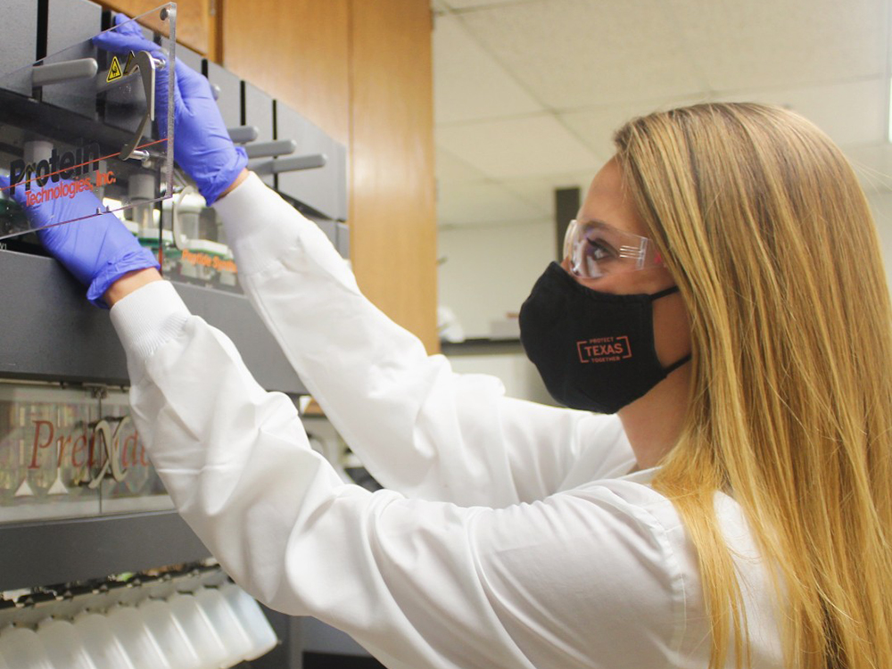 woman in lab wearing coat and texas face mask