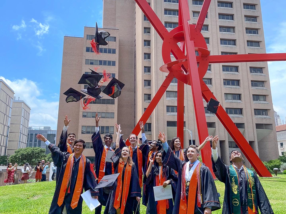 Group of students in graduation gowns throwing caps in the air