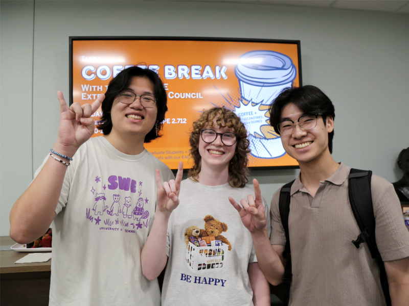 Chemical engineering students doing hook'em hand signs in front of digital screen
